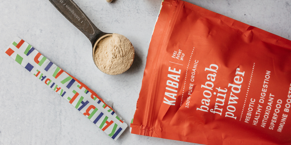 Baobab fruit powder by KAIBAE in bright red pouch tilted with a Tbsp of Baobab powder I KAIBAE