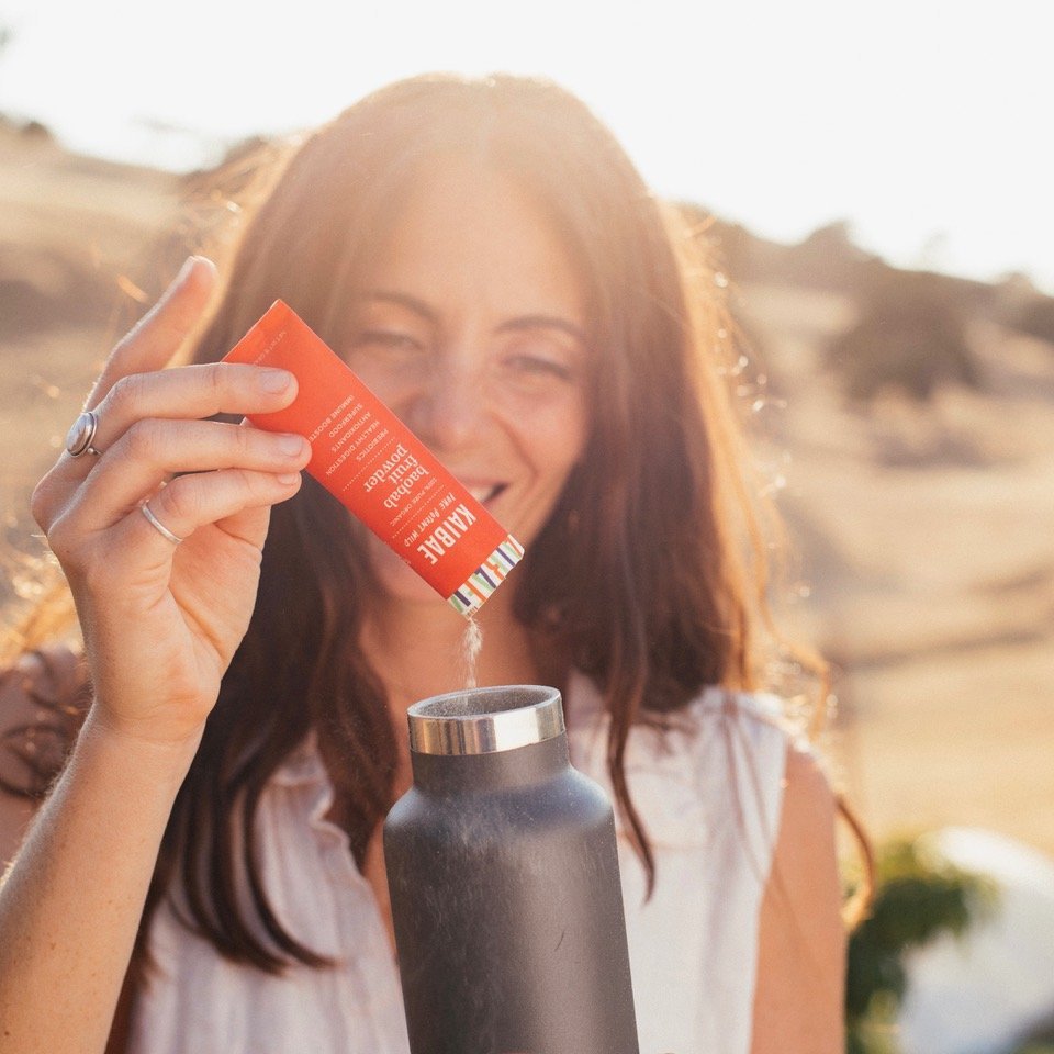 A woman adds KAIBAE Baobab on the go stick pack to water to help with hydration while hiking.