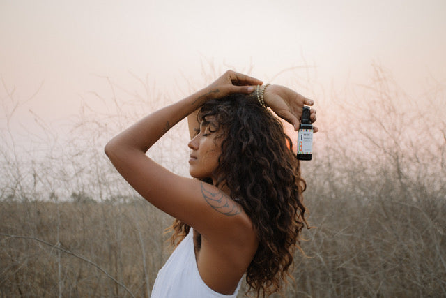 KAIBAE Baobab oil head to toe in the hands of Chante  with glowing skin and flowing hair standing in a field. 