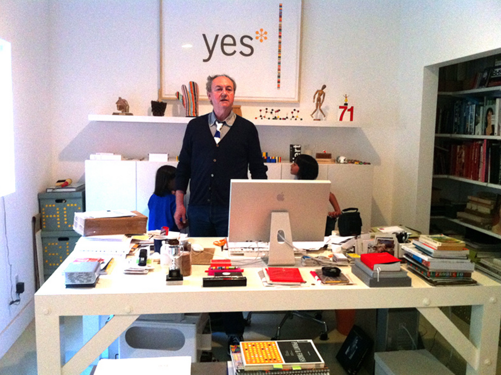Clive Piercy famous graphic designer standing at his desk with all his whimsical designs and collection of objects