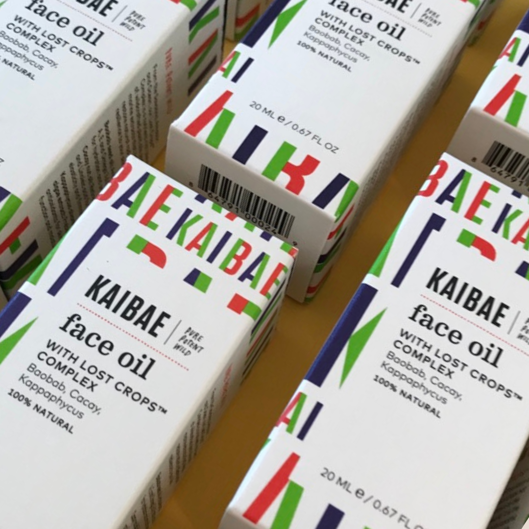 A photo of multiple boxes of KAIBAE face oil. The white boxes feature colorful, modern typography and designs. Each box reads “KAIBAE face oil with lost crops complex” and highlights the product being natural and providing hydration for your skin.