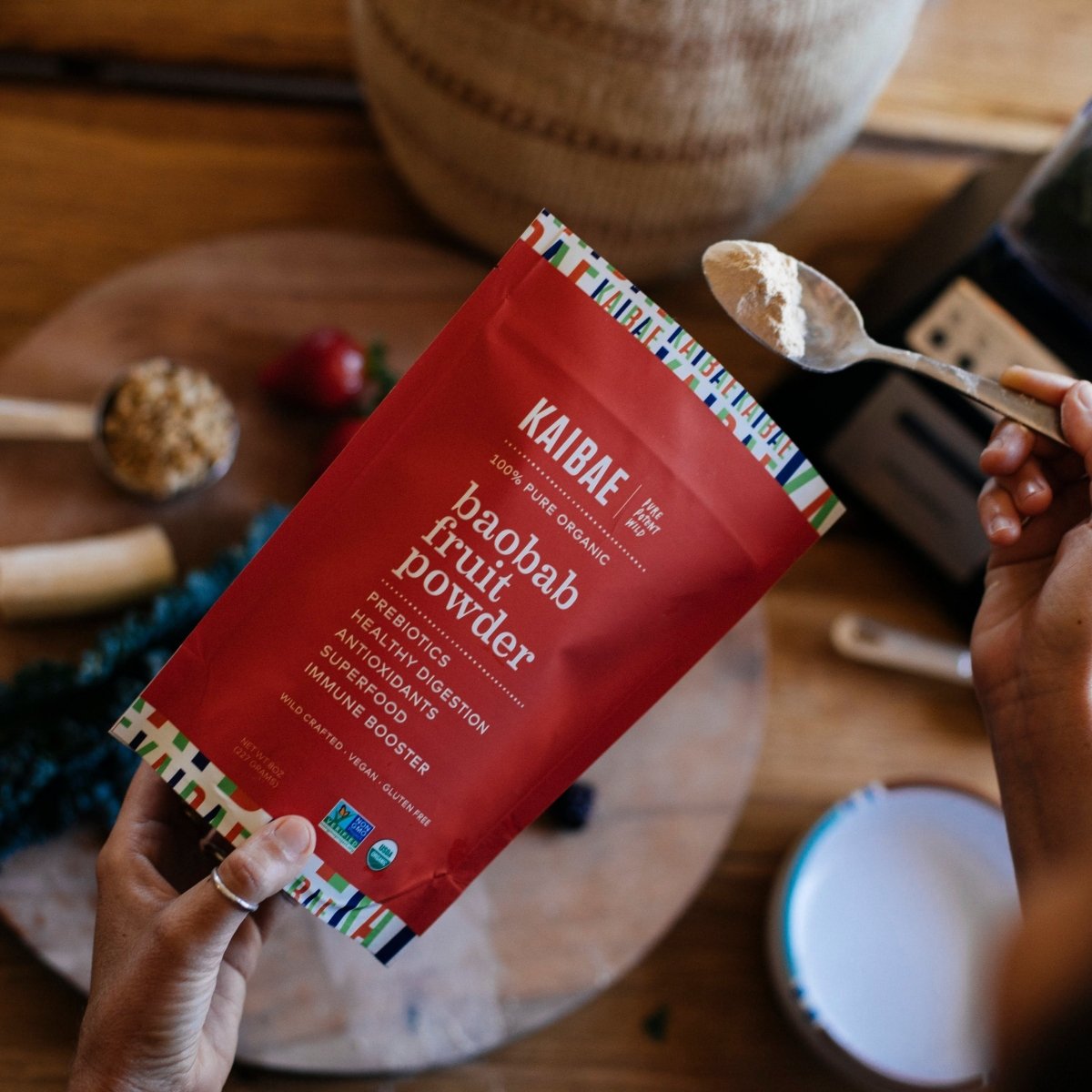 An individual scoops KAIBAE Baobab powder from a red pouch into a cup to make a smoothis. 